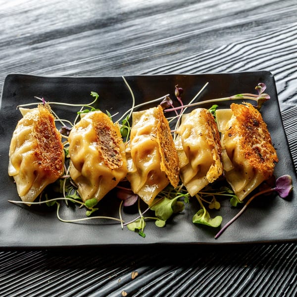 Five golden-brown Susukino Ramen Bar gyoza with crispy edges and microgreens on a black plate.