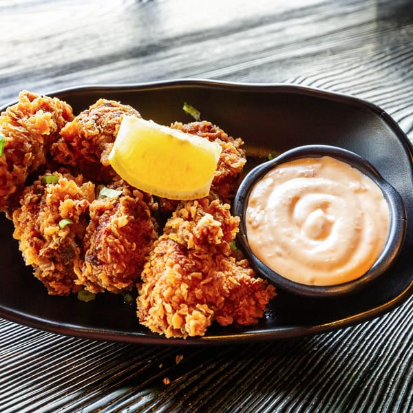 Crispy fried chicken pieces with a lemon wedge and a side of creamy sauce on a black plate.