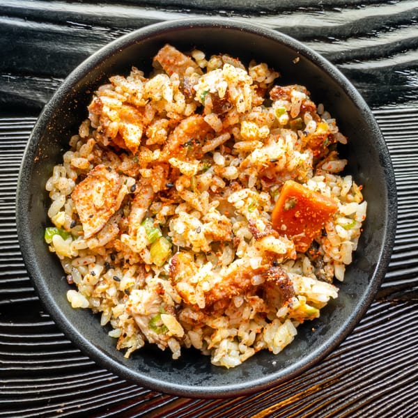 A close-up of Susukino Ramen Bar's fried rice with chicken, vegetables, and red spice in a black bowl.