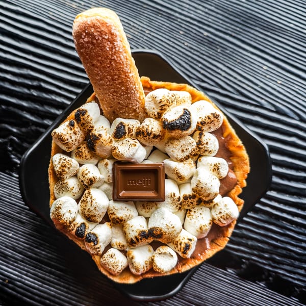 A dessert with toasted marshmallows, a Meiji chocolate square, and a ladyfinger cookie.