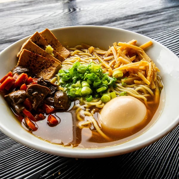 A bowl of Susukino Ramen with noodles, tofu, mushrooms, carrots, green onions, and a boiled egg.