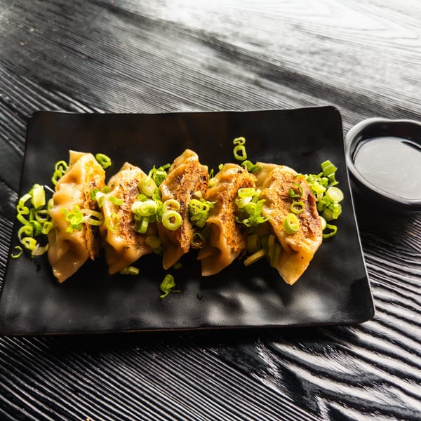 Pan-fried gyoza dumplings topped with chopped green onions, served with a side of dipping sauce.
