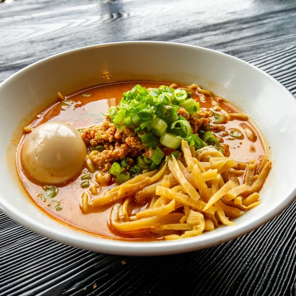 Spicy ramen bowl with ground pork, green onions, bamboo shoots, and a soft-boiled egg.